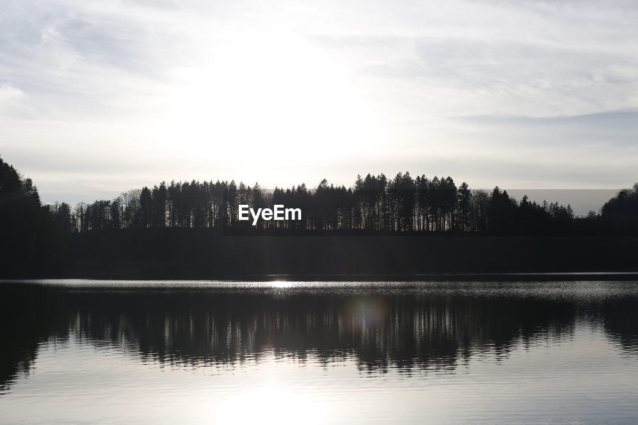 Silhouette trees by lake against sky during sunset