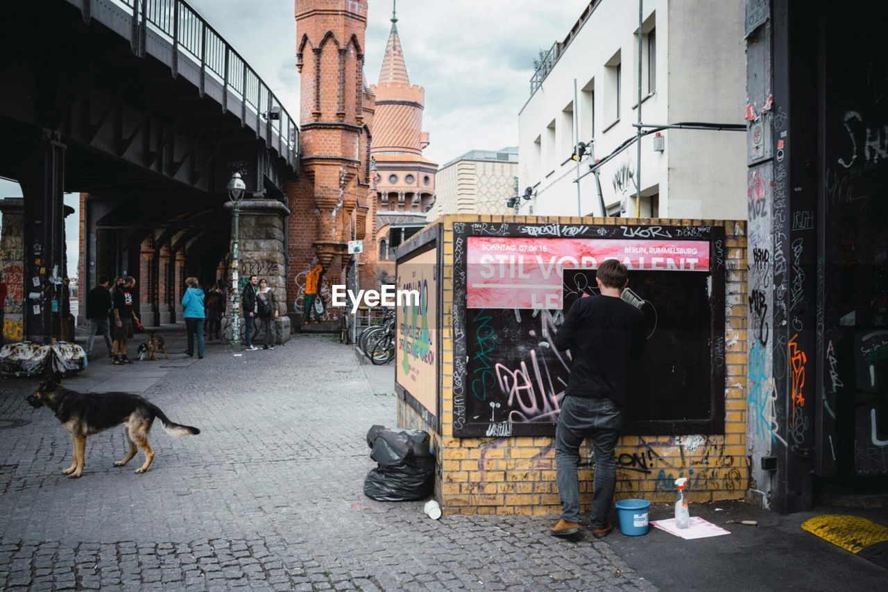 Rear view of man painting on graffiti wall in city