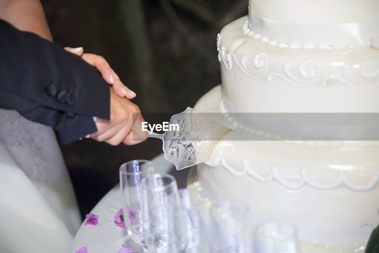 Cropped image of bride and groom cutting wedding cake