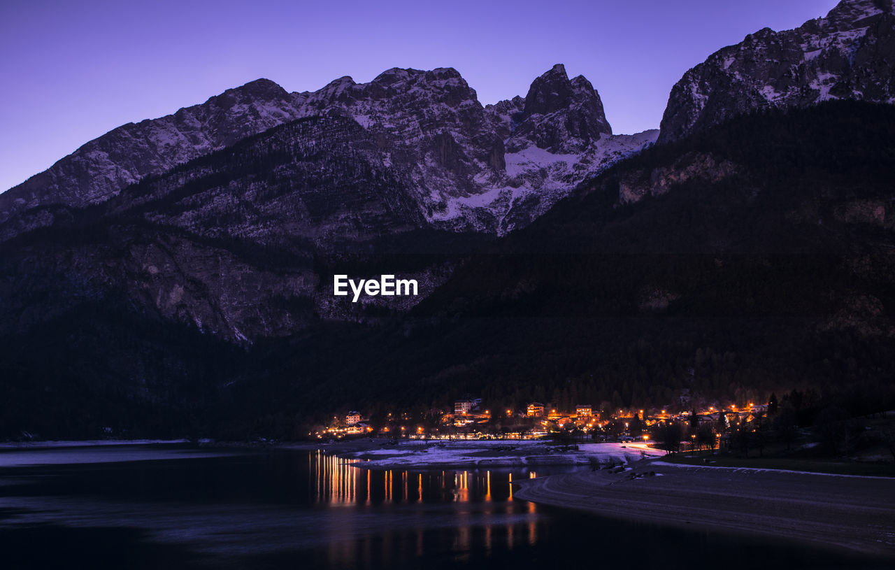 Scenic view of lake by mountains against sky at night