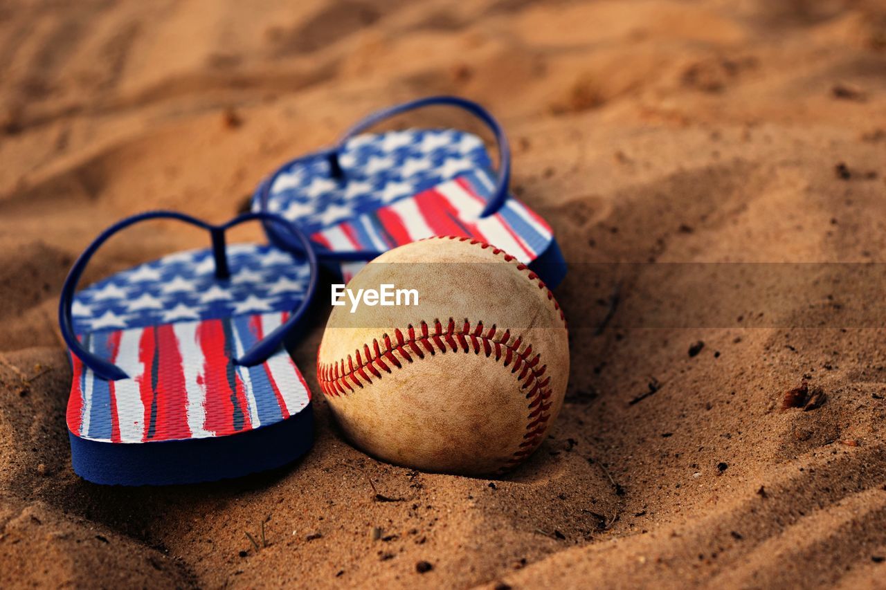 Close-up of baseball and flip-flops on sand