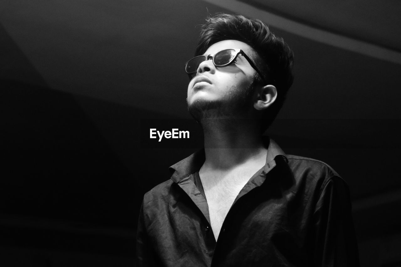 Close-up of young man wearing sunglasses while standing in darkroom