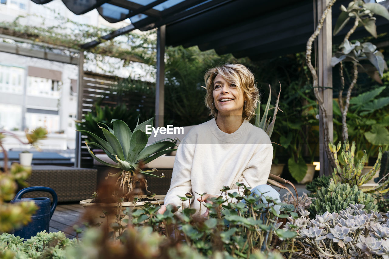 Smiling woman looking away amidst plant at rooftop garden