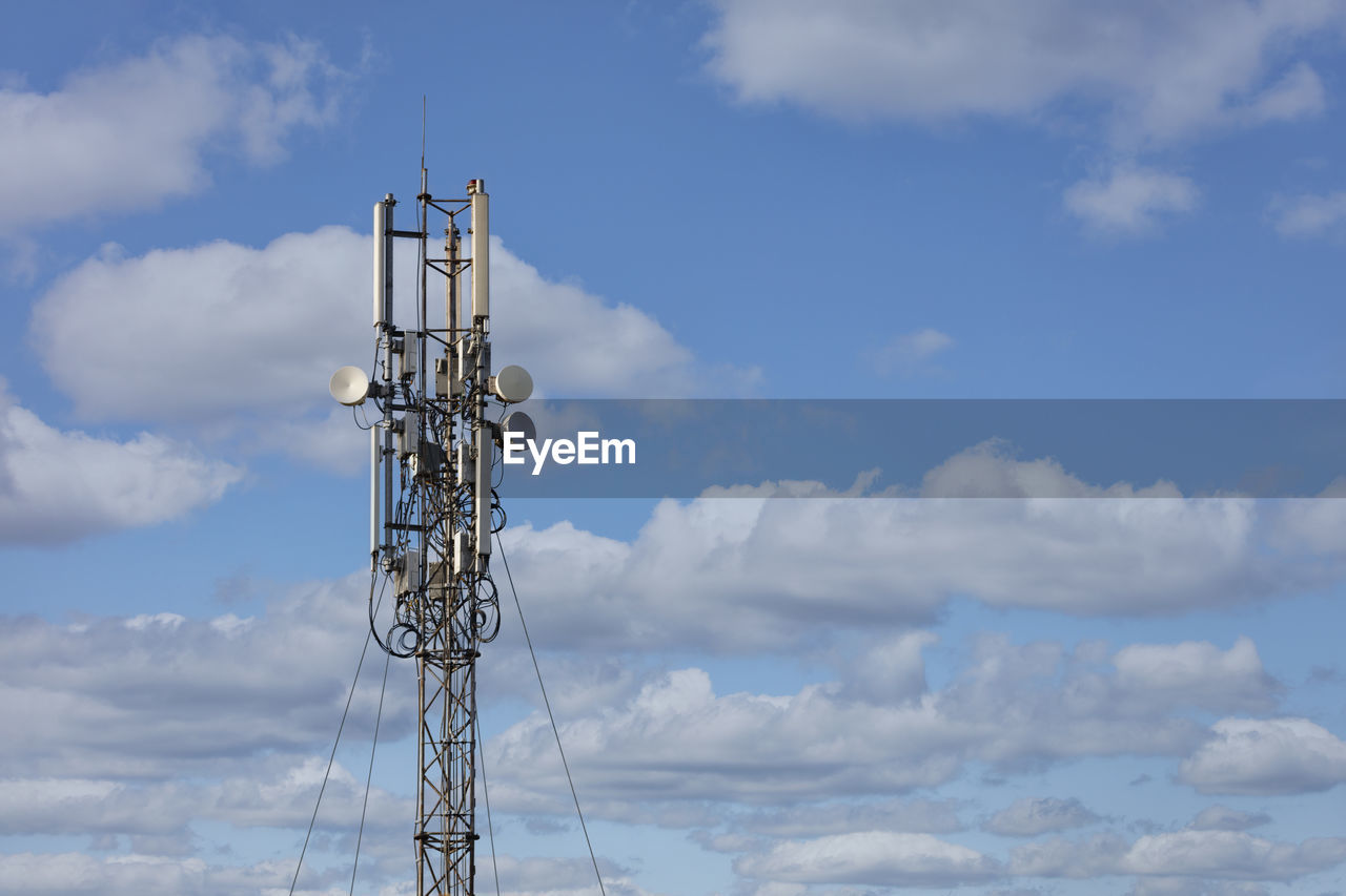 Cellular antennas on a metal mast against a blue cloudy sky.