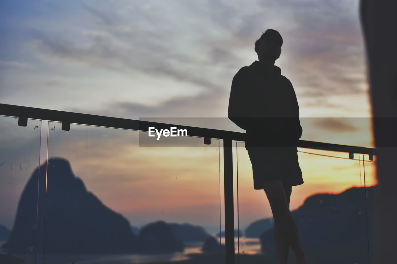 Low angle view of silhouette man standing at railing against sky