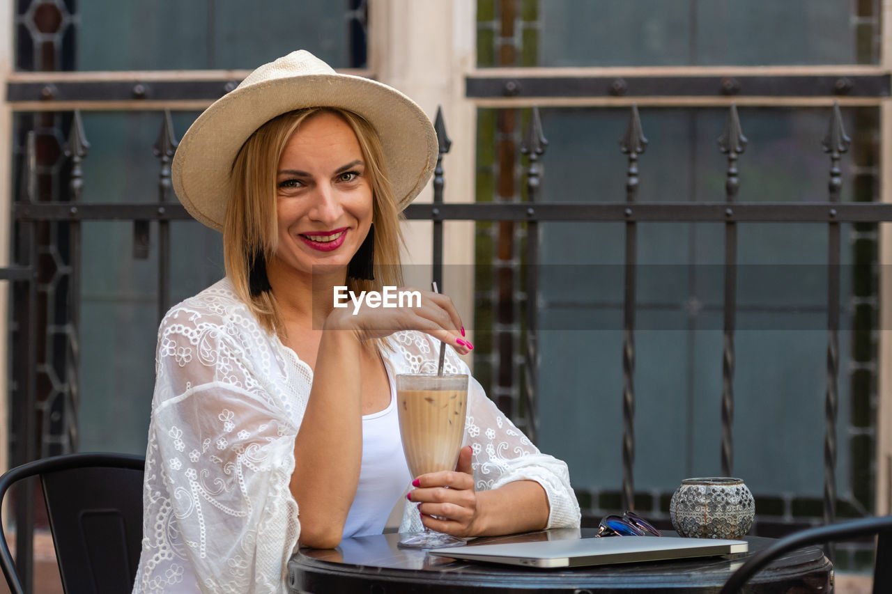 Portrait of smiling woman with coffee sitting at outdoor cafe