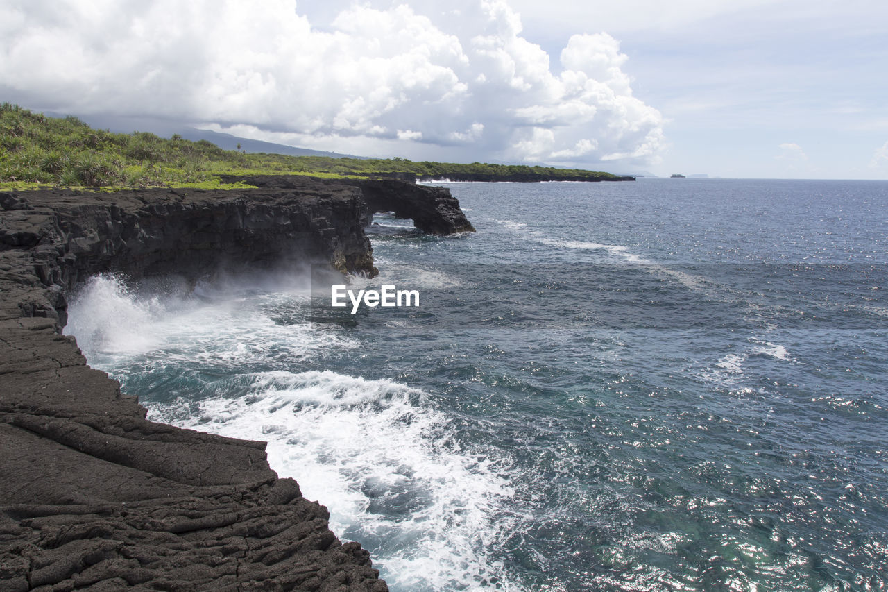 Volcanic coastal cliffs with blue waves breaking during sunny day