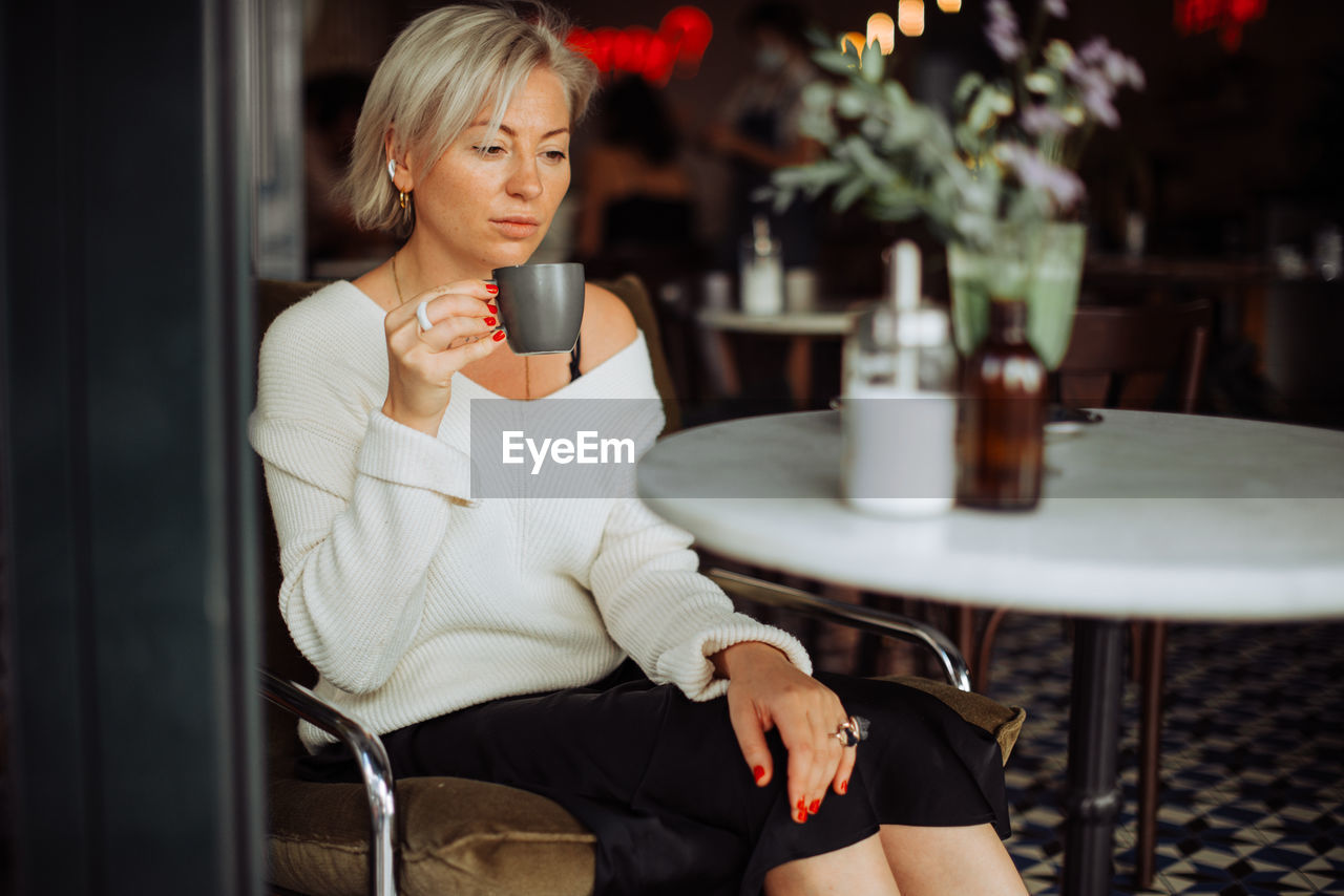 Woman drinking coffee looking sad while sitting alone at table in cafe