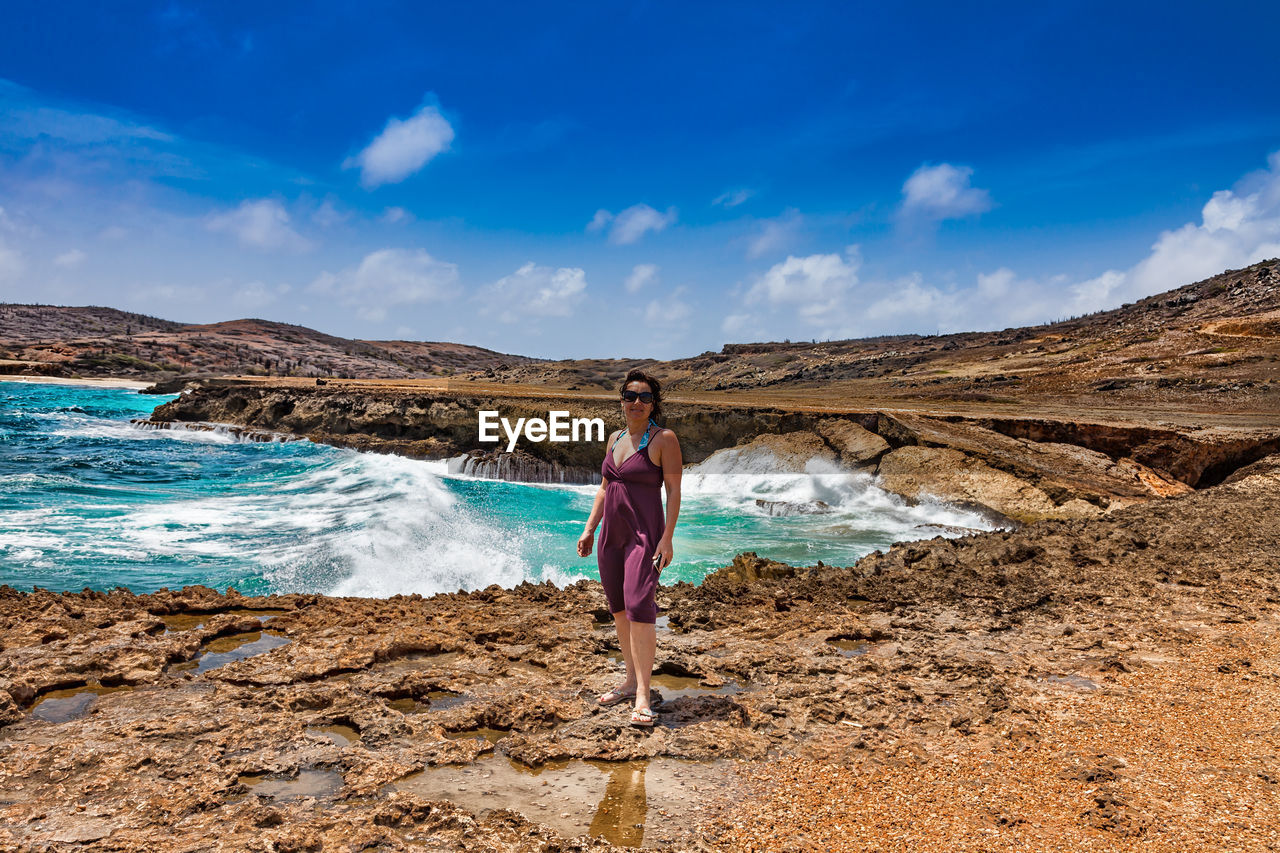 Full length of woman standing on rock by sea against sky