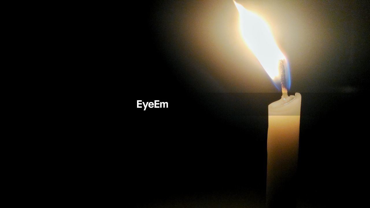 CLOSE-UP OF LIT CANDLE IN DARK ROOM