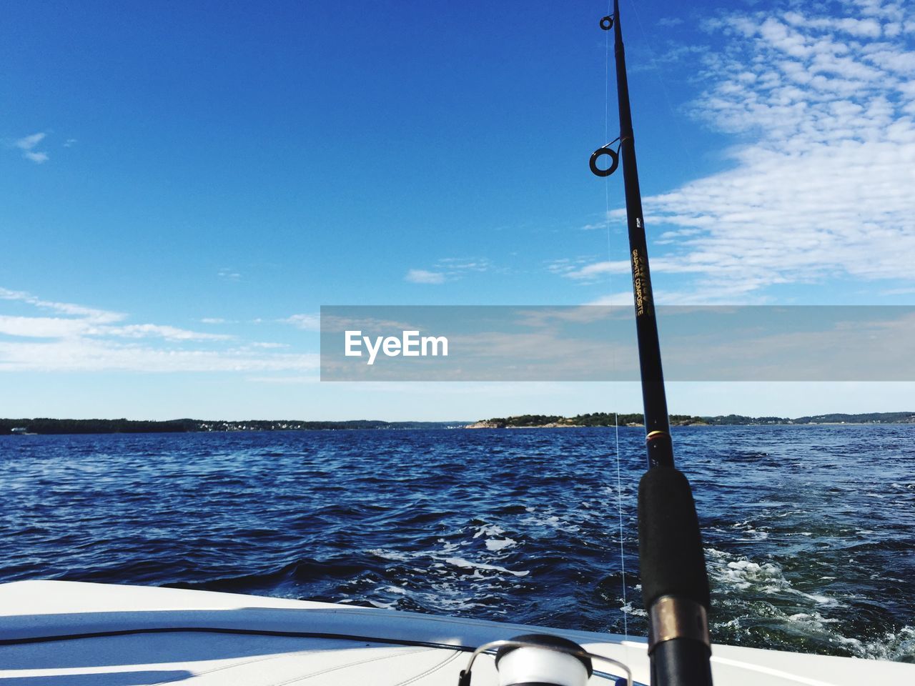 Cropped image of fishing rod and boat in sea against sky