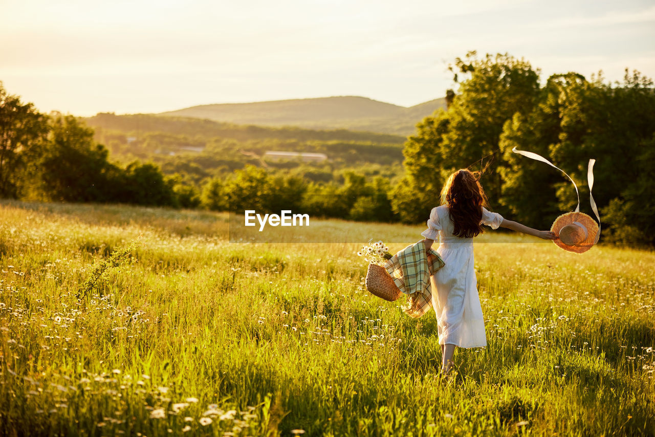 rear view of woman with arms raised standing on grassy field