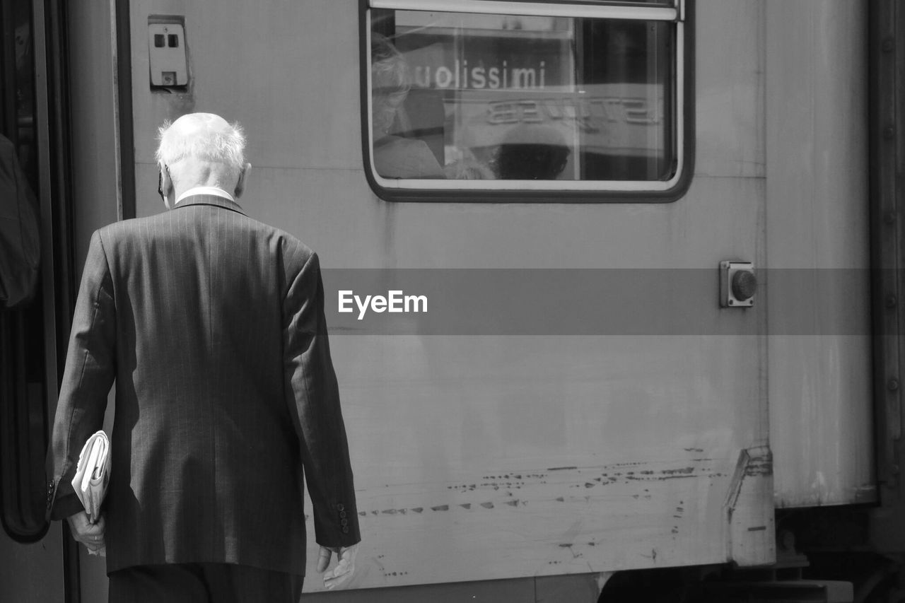 REAR VIEW OF MAN STANDING ON TRAIN AT RAILROAD STATION