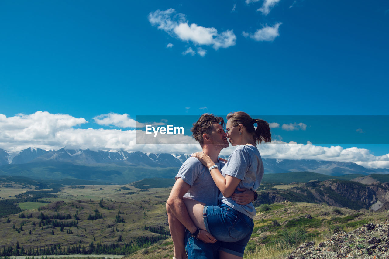 REAR VIEW OF COUPLE KISSING AGAINST MOUNTAIN