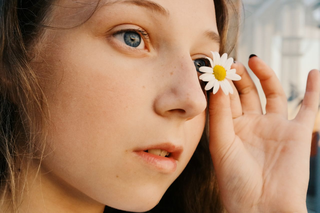 Close-up of a girl holding a daisy flower near her eye