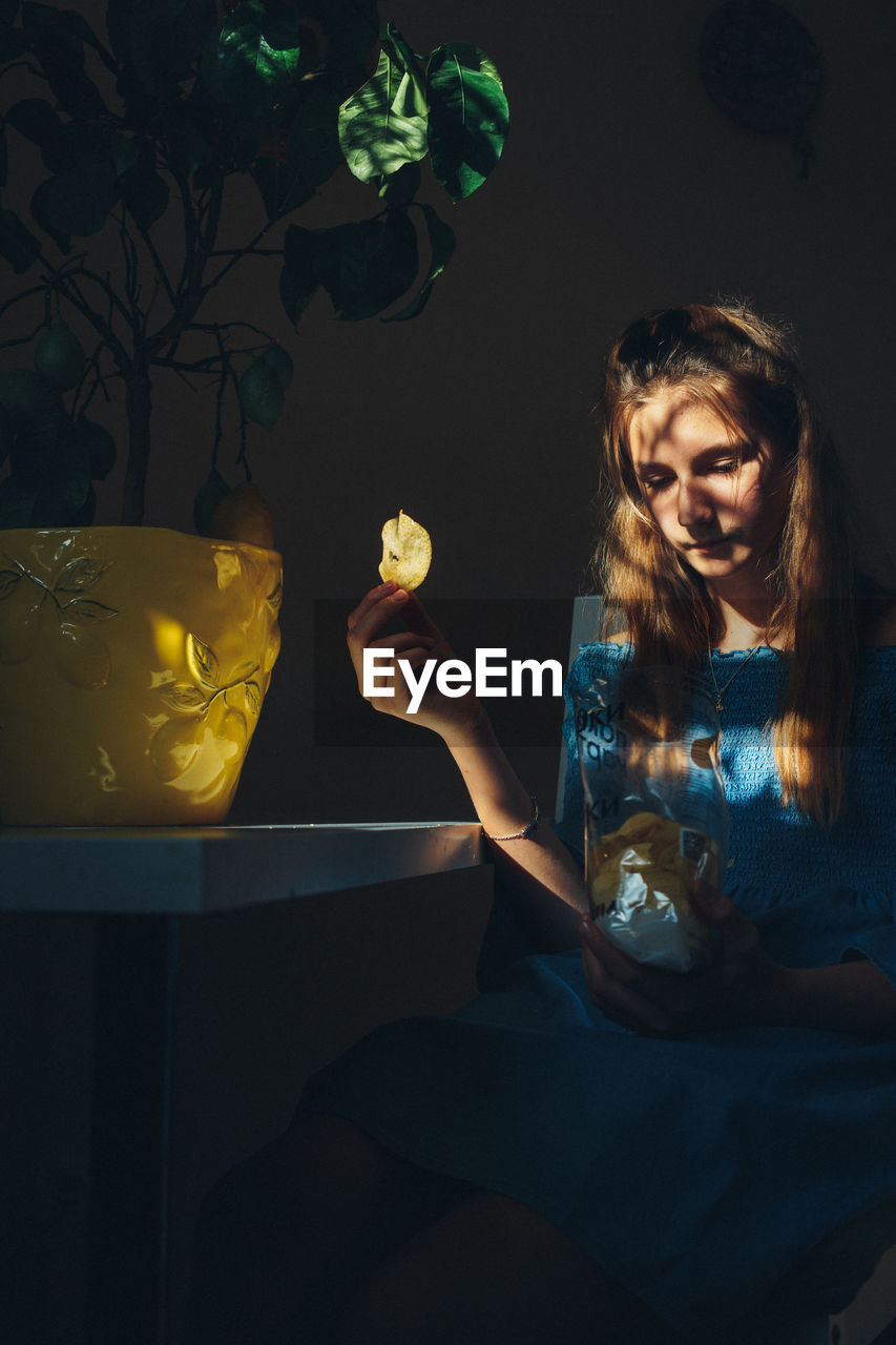 Girl holding potato chip sitting at home