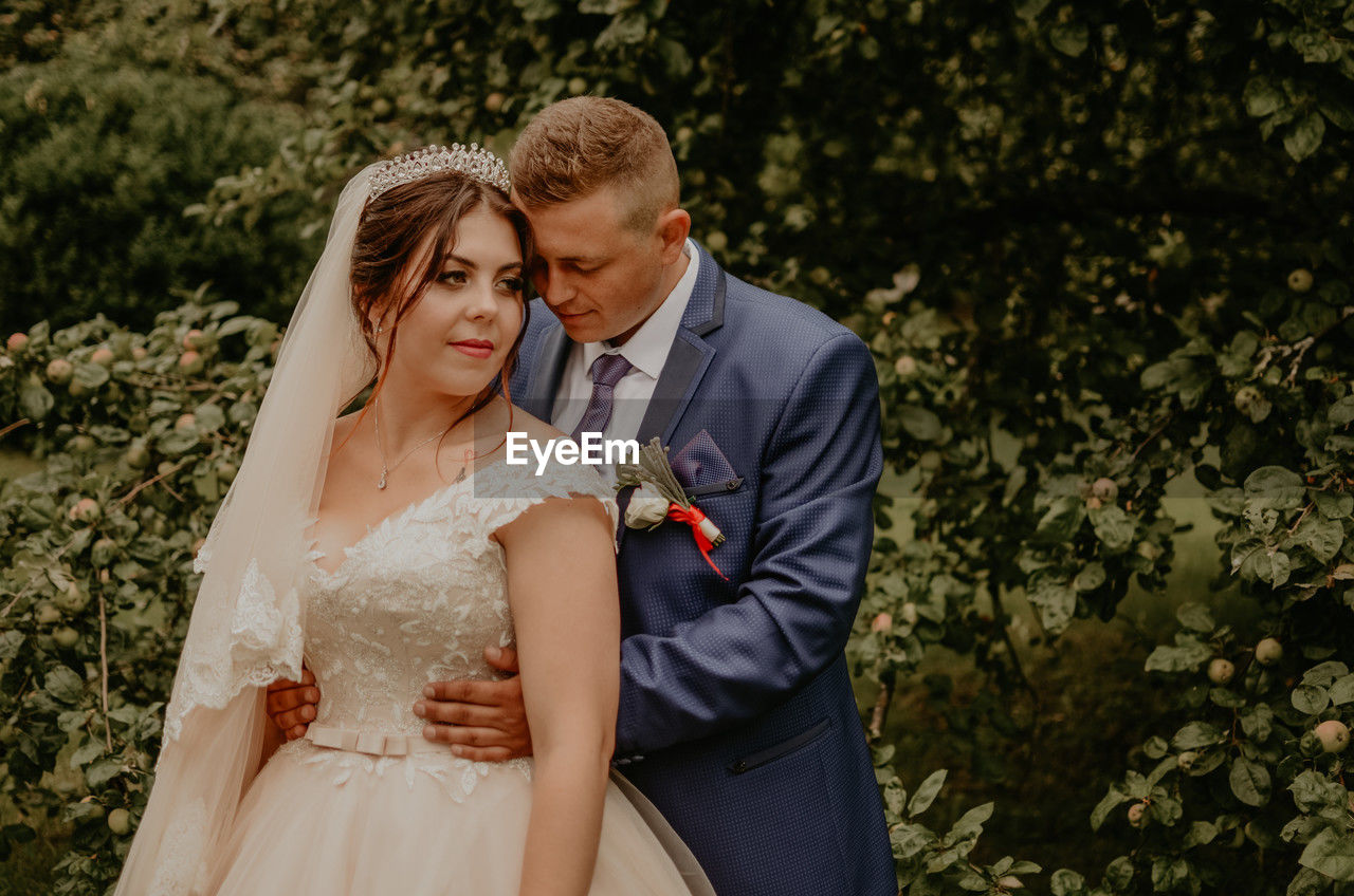 portrait of bride and bridegroom standing against trees