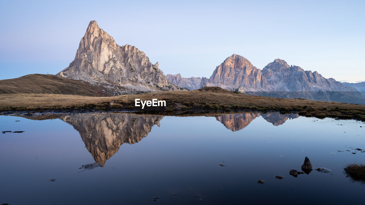 Rocky mountains reflected in small still pond serving as a mirror during sunrise , dolomites, italy