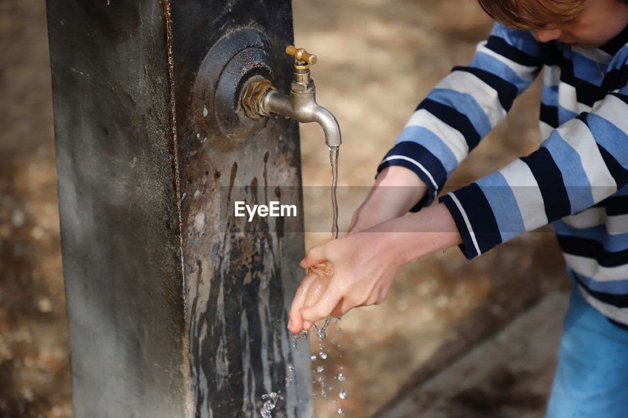 Midsection of boy washing hands at outdoors