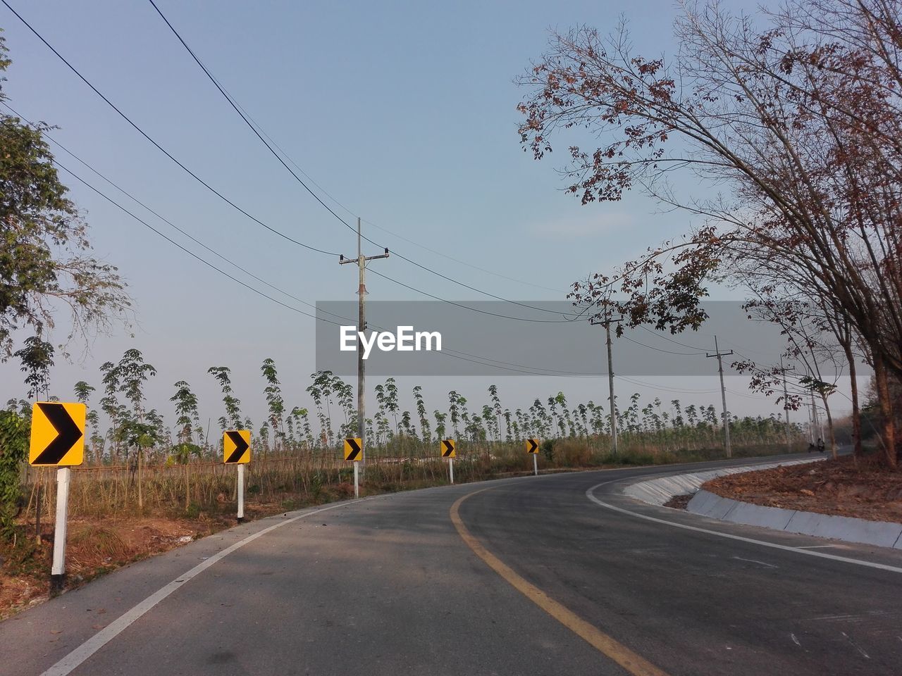 road, sign, transportation, sky, lane, tree, highway, road sign, nature, residential area, symbol, electricity, plant, communication, road marking, no people, cable, street, city, infrastructure, marking, road surface, the way forward, day, outdoors, technology, clear sky, asphalt, electricity pylon, yellow, guidance, landscape, empty road, power line, travel, mode of transportation