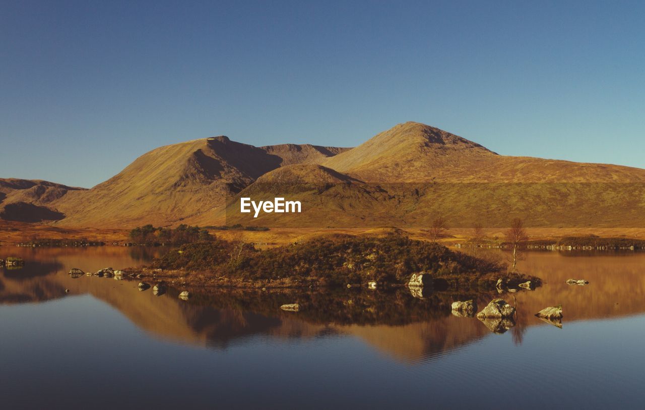 Scenic view of lake and mountains against clear blue sky