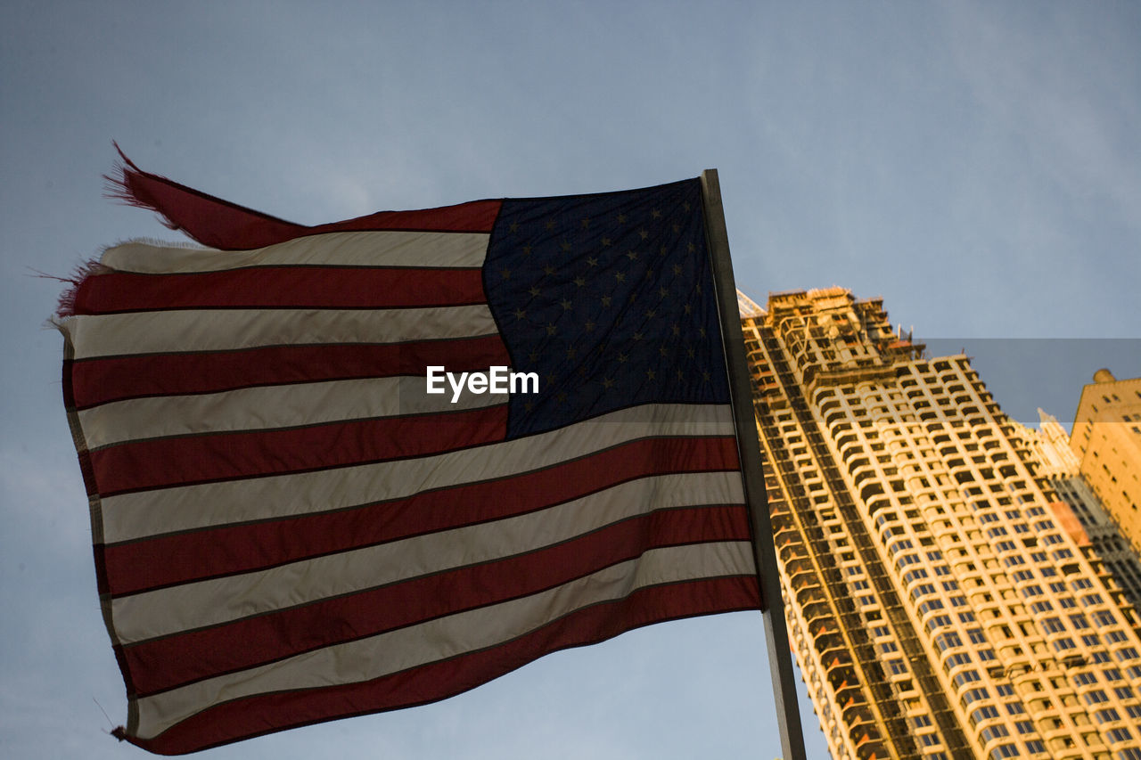 Low angle view of usa flag against sky with skyscraper.