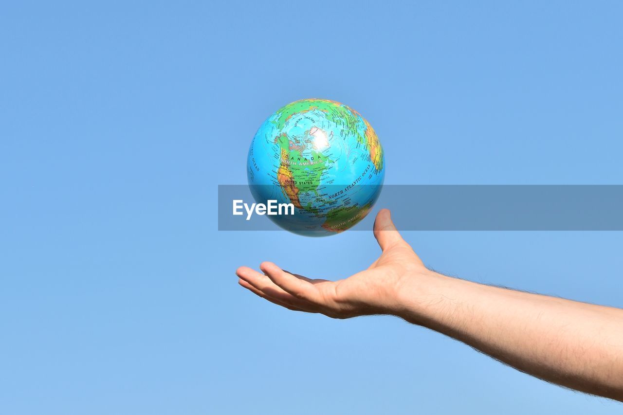 Cropped hand of man reaching globe against clear blue sky