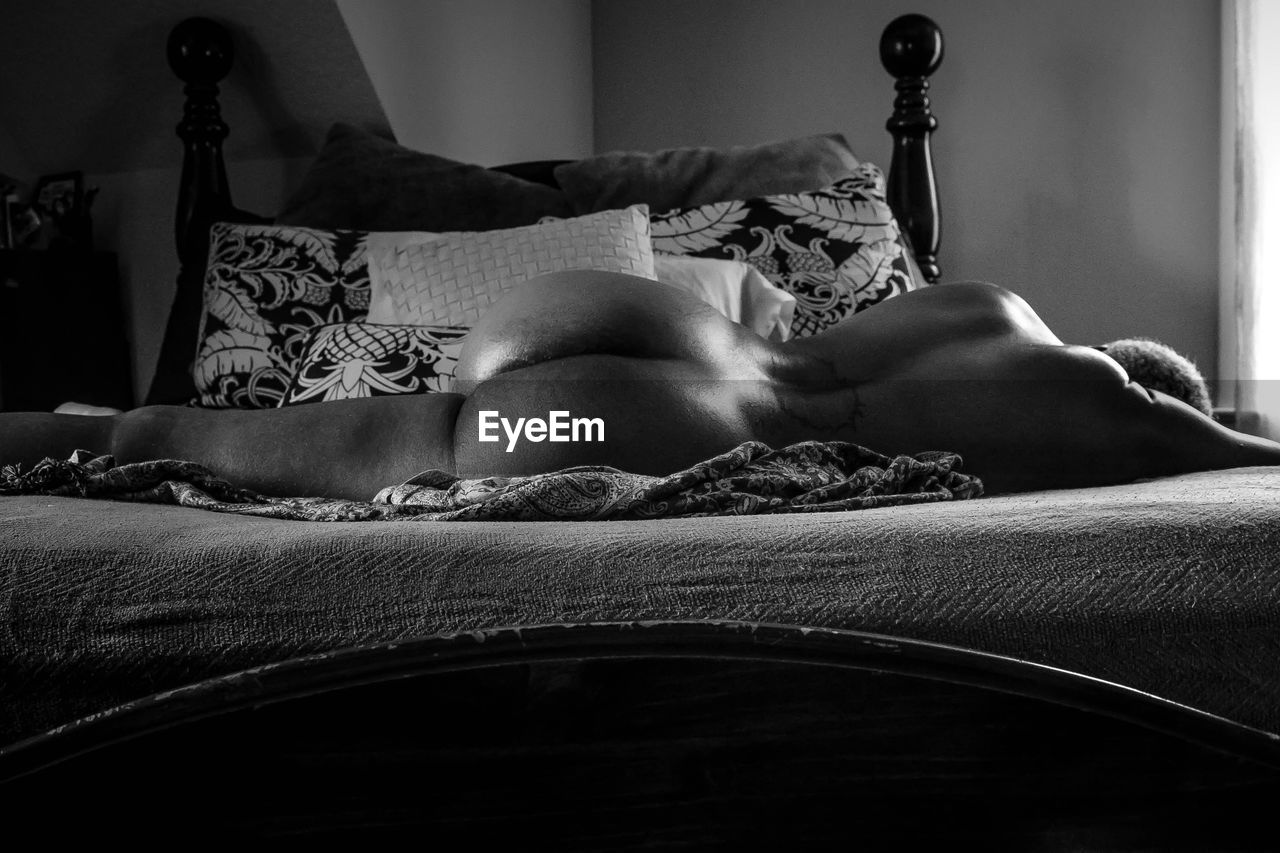 Rear view of naked person sleeping on bed at home