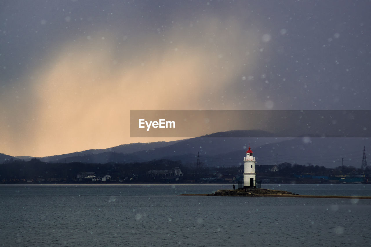 Lighthouse by sea against sky at night