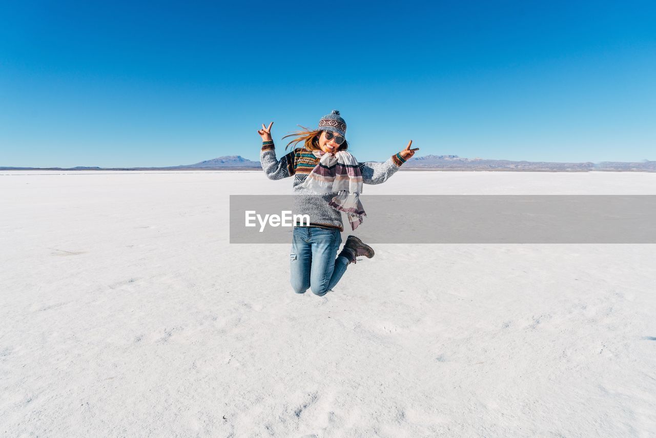 Portrait of young woman jumping on desert against clear blue sky