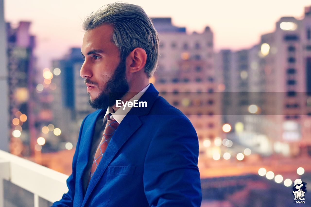 Young businessman standing against illuminated city