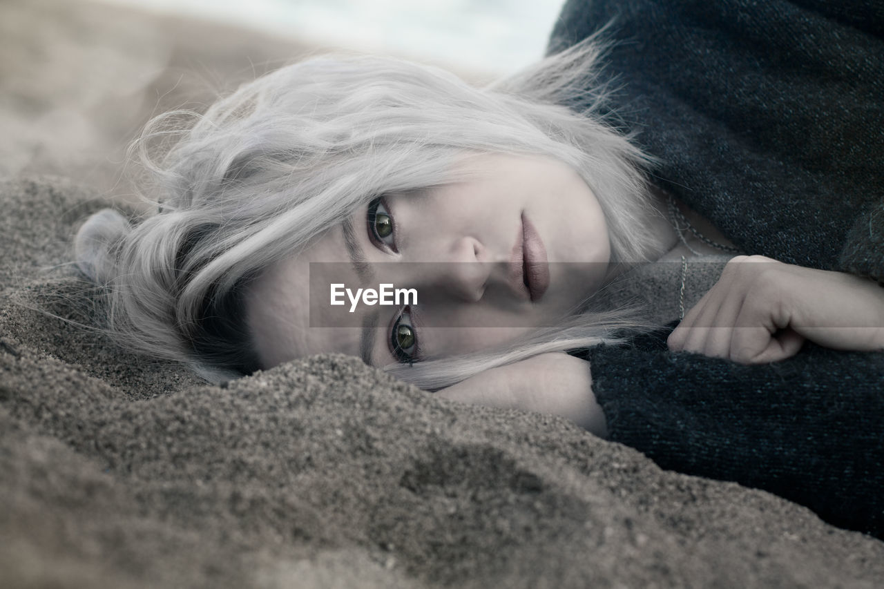 Surface level of thoughtful woman lying on sand at beach