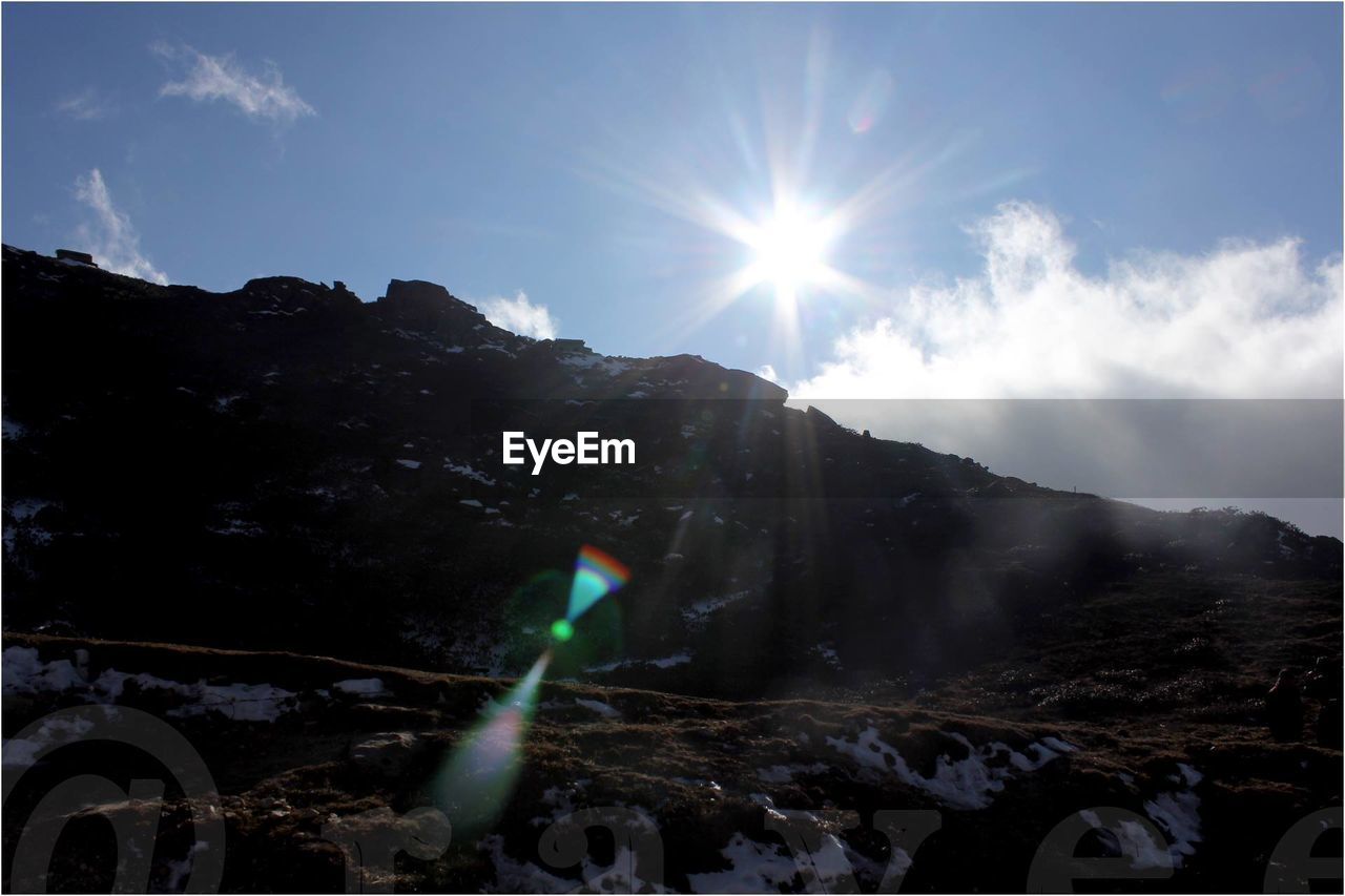 SUN SHINING THROUGH CLOUDS OVER MOUNTAINS