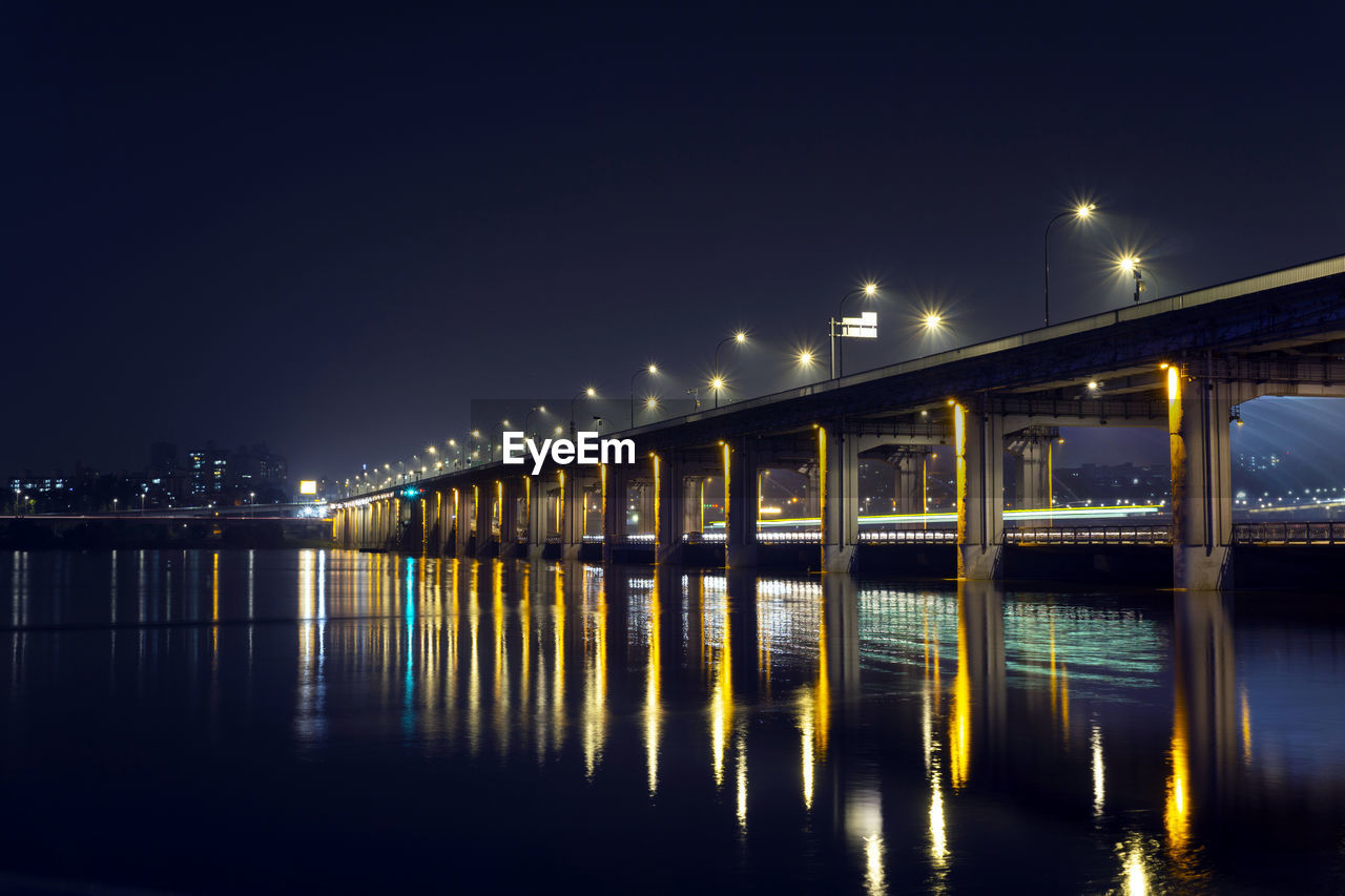 illuminated bridge over river against clear sky at night