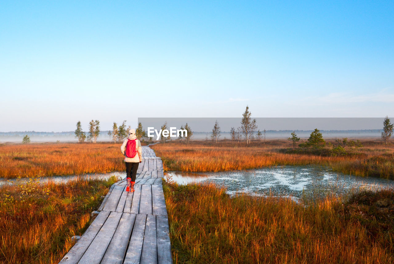 REAR VIEW OF MAN STANDING IN WATER AGAINST SKY