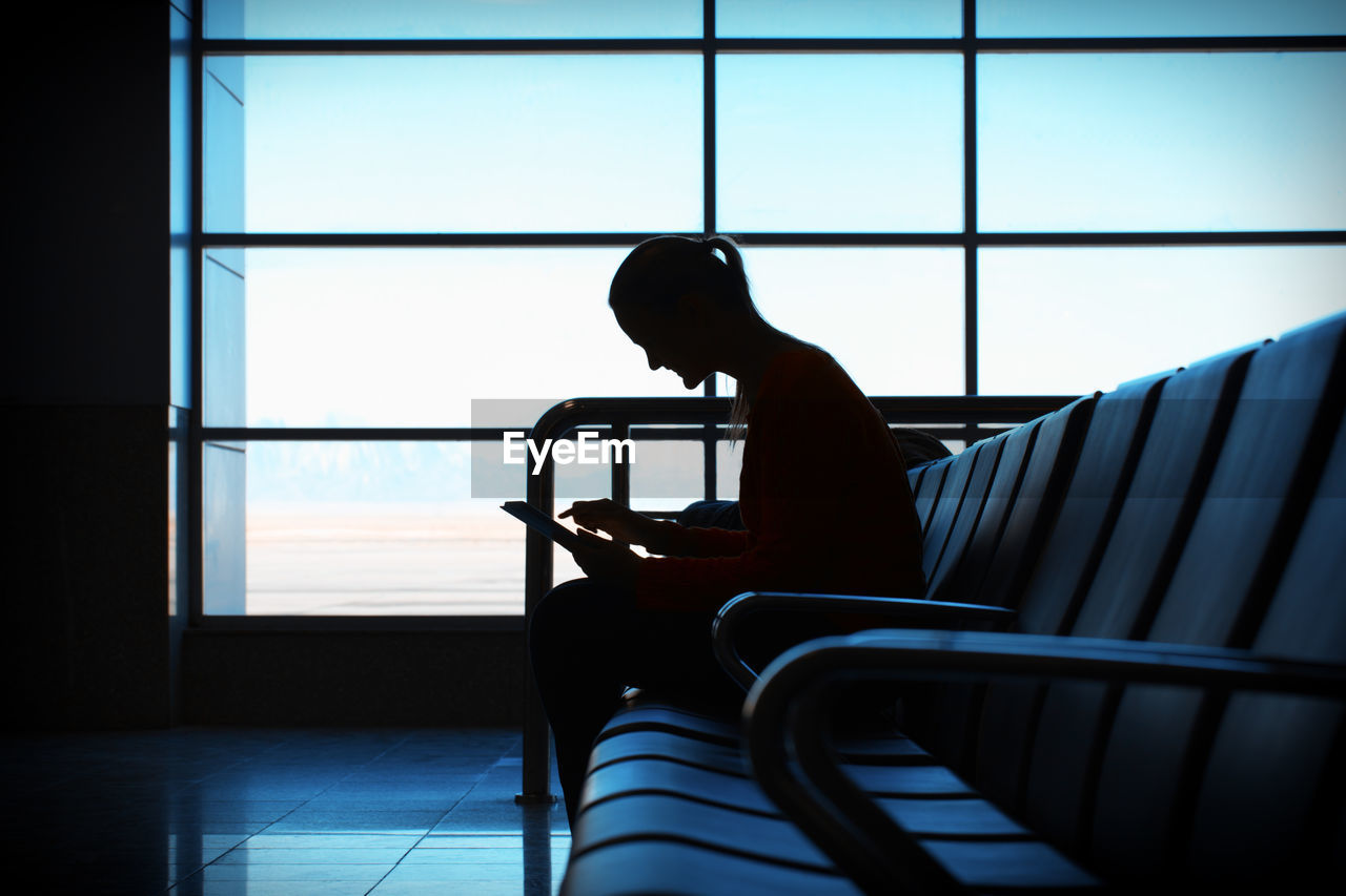 Woman using digital tablet while sitting on chair in airport lobby