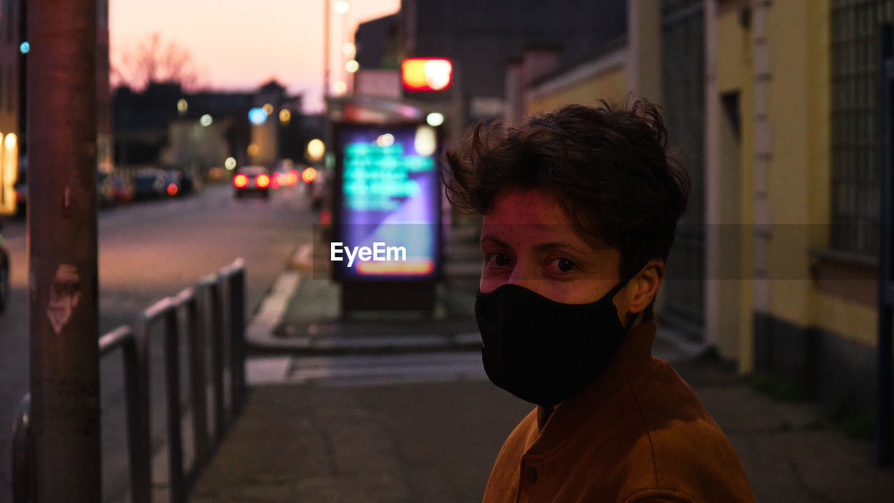 Portrait of woman with short hair standing on street at night wearing a mask