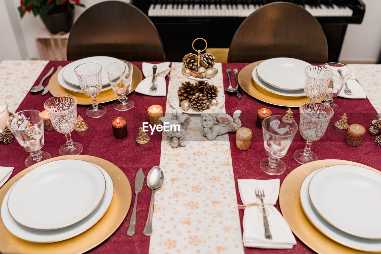 From above of table setting with glasses and cutlery near plates decorated with candles and cones for christmas celebration