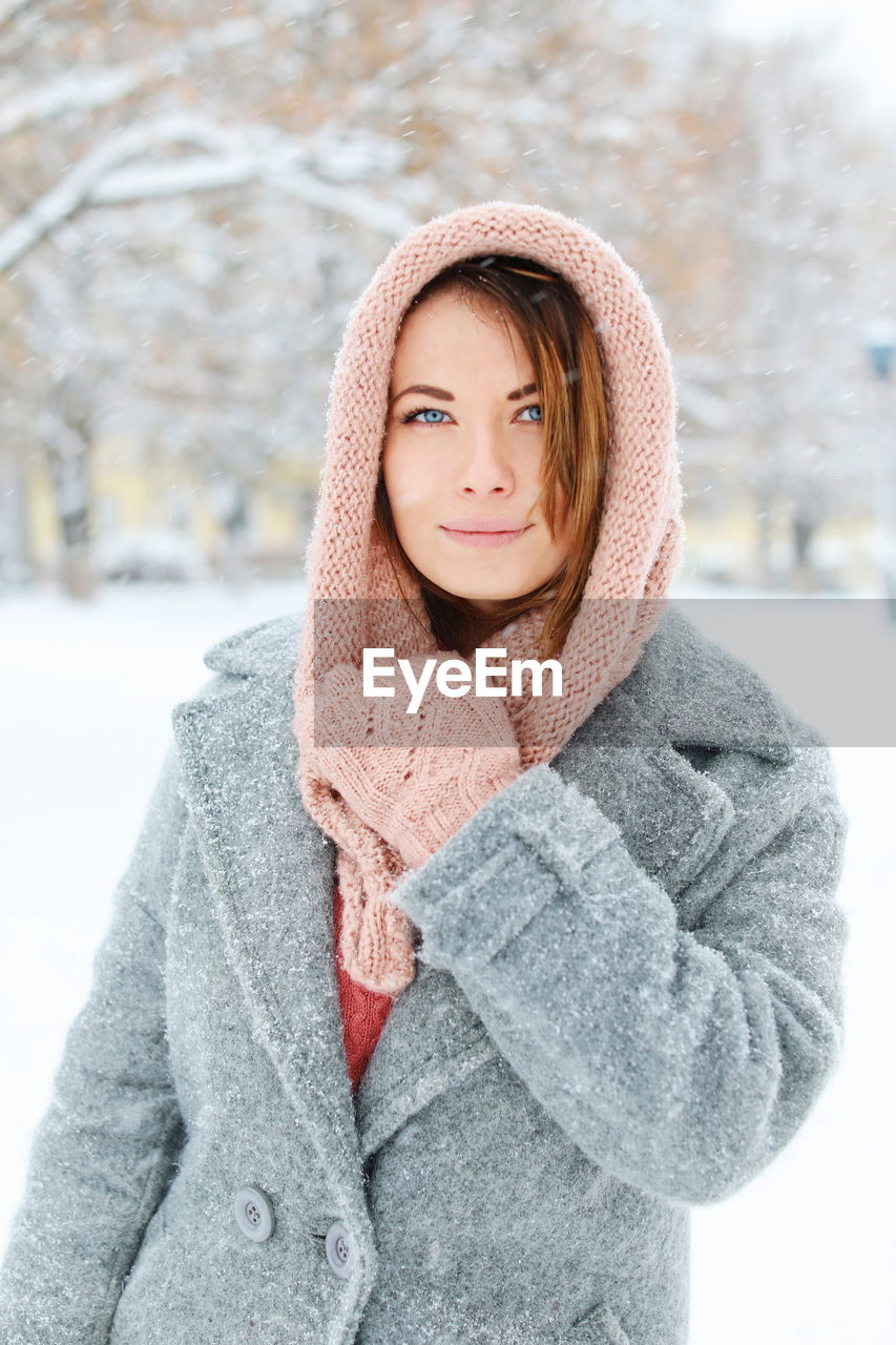 Portrait of smiling young woman standing against trees during winter