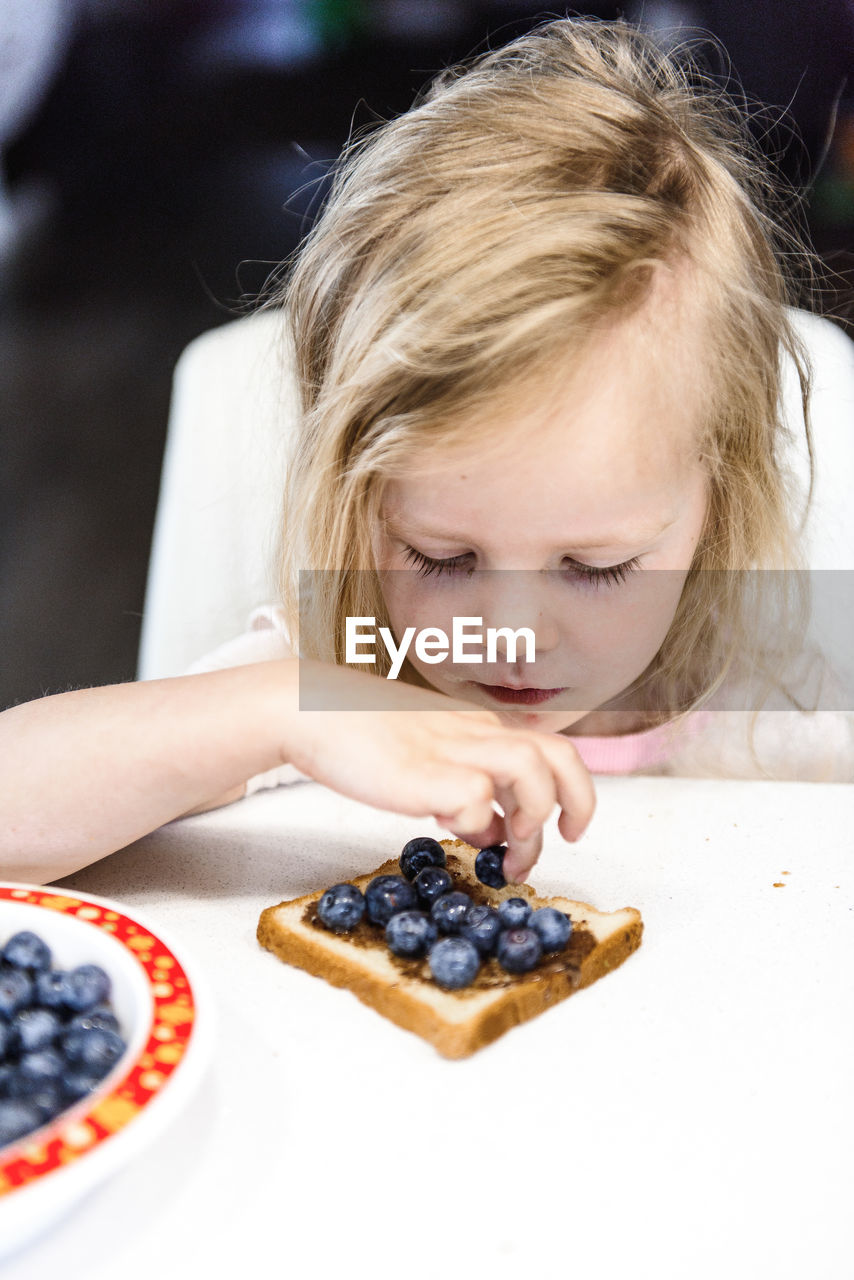 A little cute girl is eating her breakfast toast with blueberries