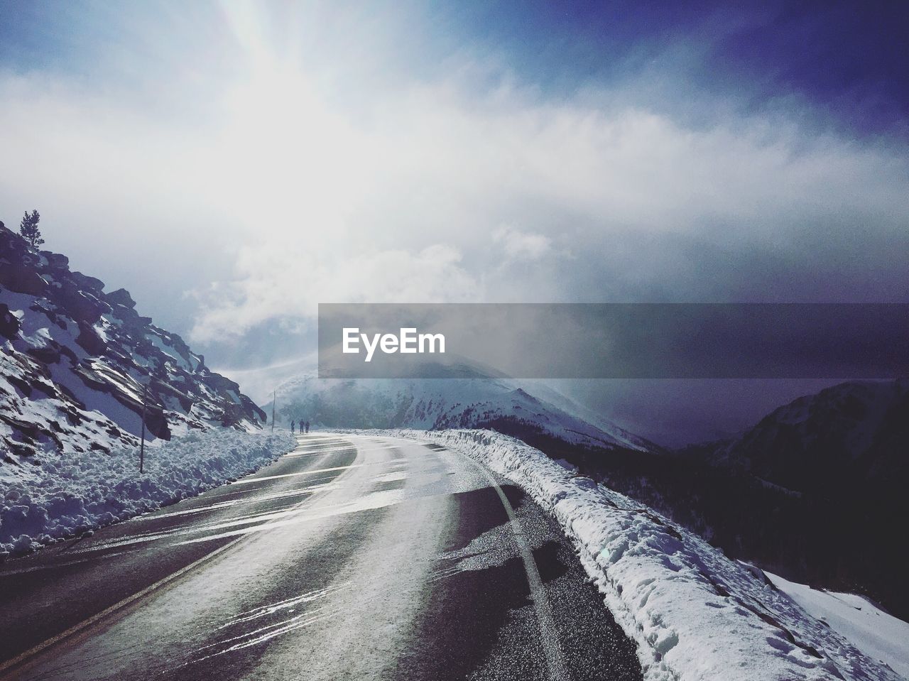 Empty road by mountain against sky during winter