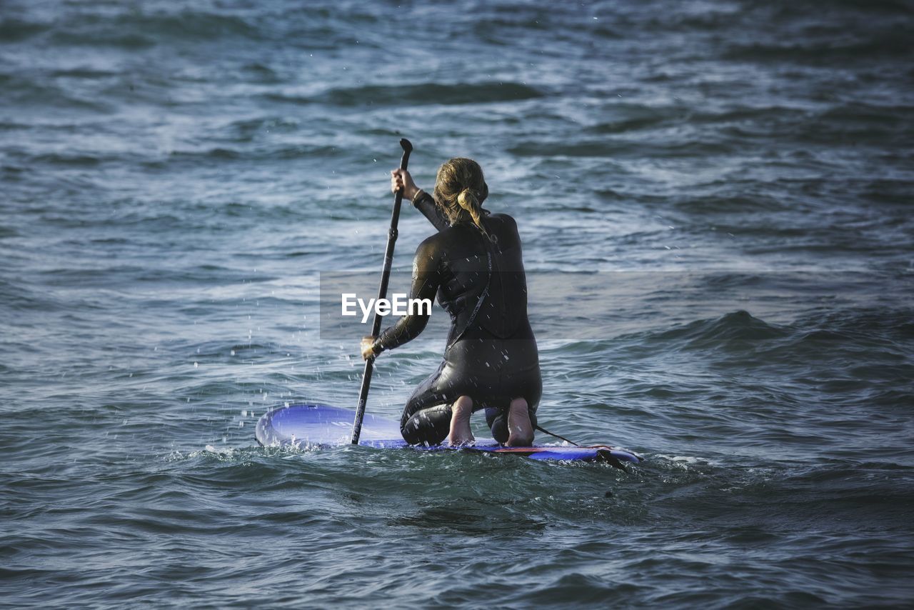 Rear view of woman paddleboarding in sea