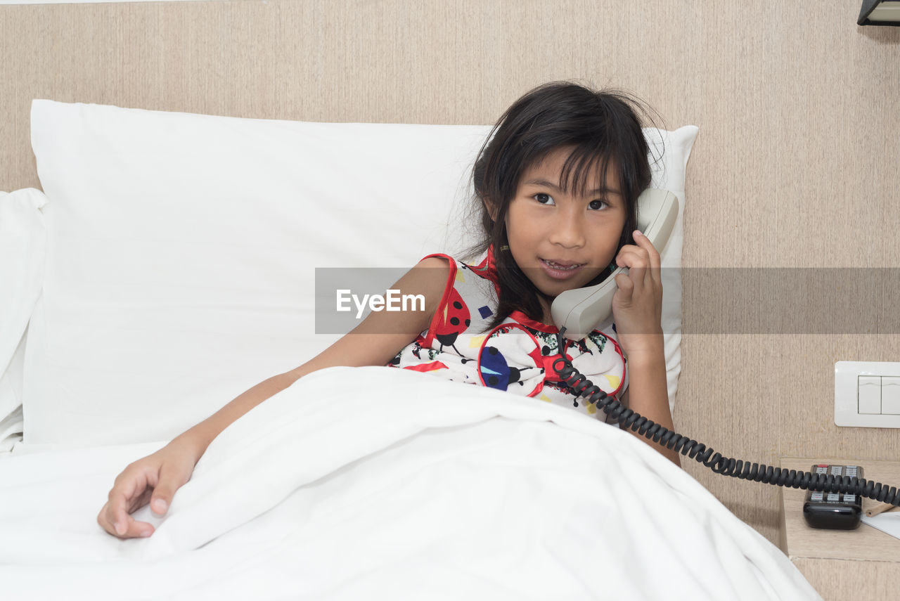 Portrait of girl talking on phone while lying in bed at home