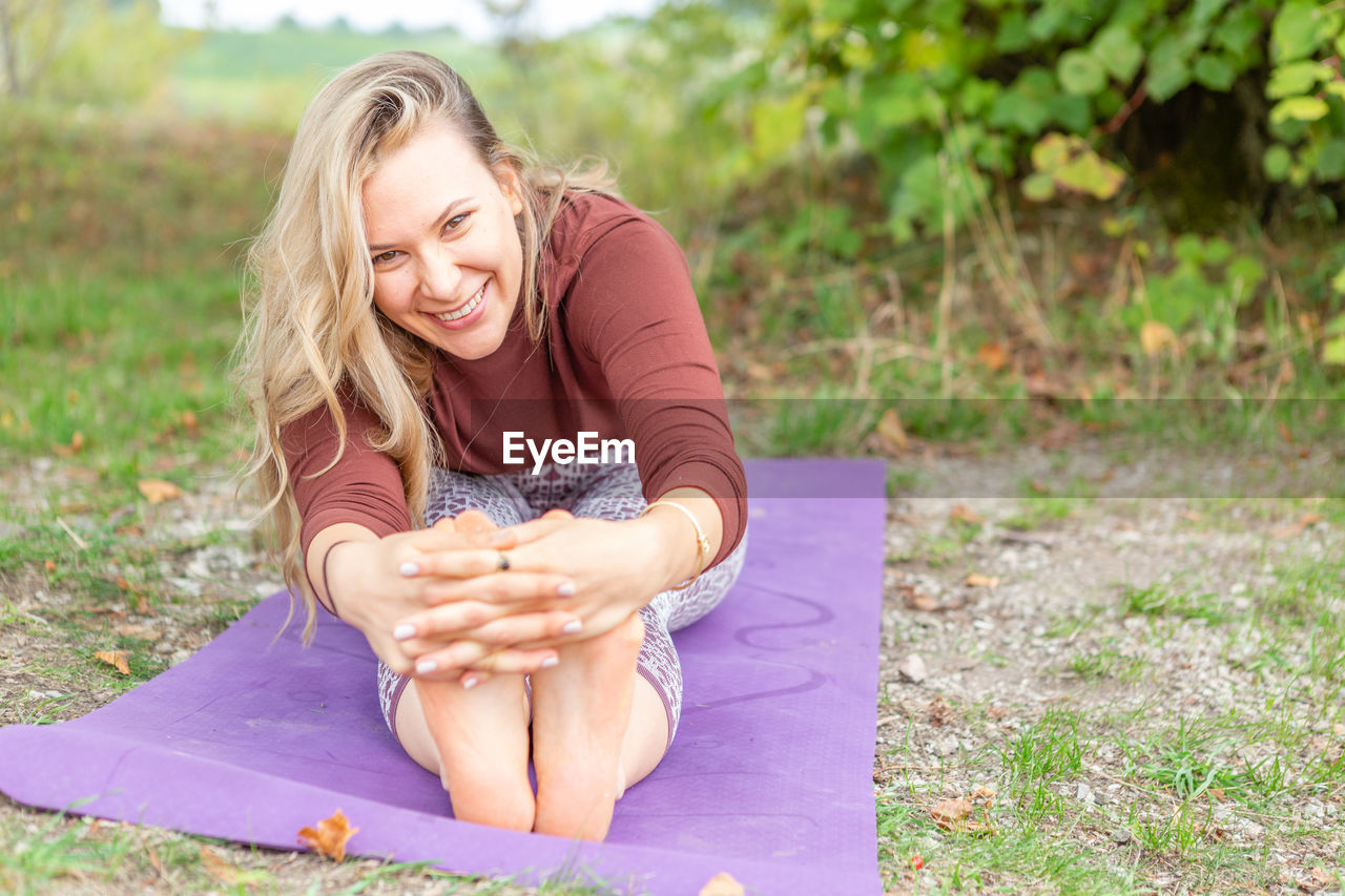 women, one person, adult, smiling, blond hair, sitting, grass, happiness, lifestyles, nature, emotion, long hair, relaxation, hairstyle, plant, young adult, leisure activity, clothing, wellbeing, person, portrait photography, female, full length, yoga, casual clothing, portrait, outdoors, exercising, cheerful, cross-legged, summer, human face, day, positive emotion, front view, enjoyment, field, teeth, child, land, smile, human leg, physical fitness