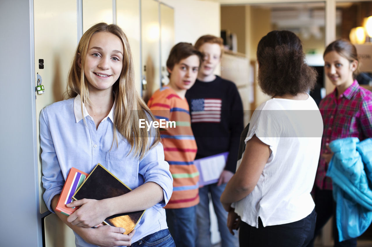 Portrait of school girl standing at locker room with friends in background