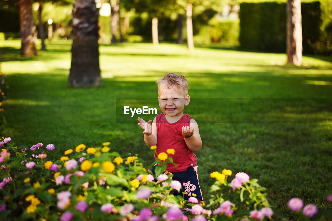 Little boy smiling in the summer in the garden near the flowers