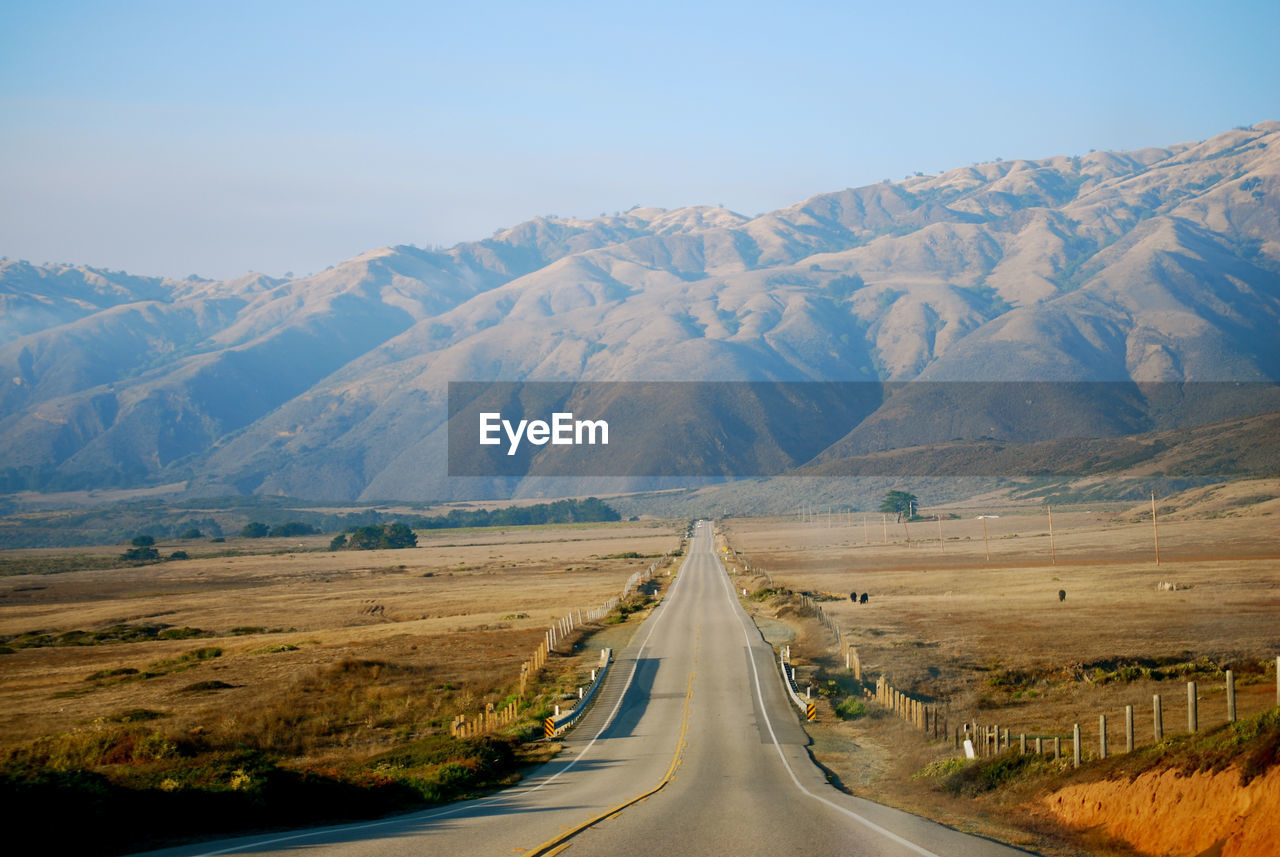 Empty road leading towards mountains against clear sky