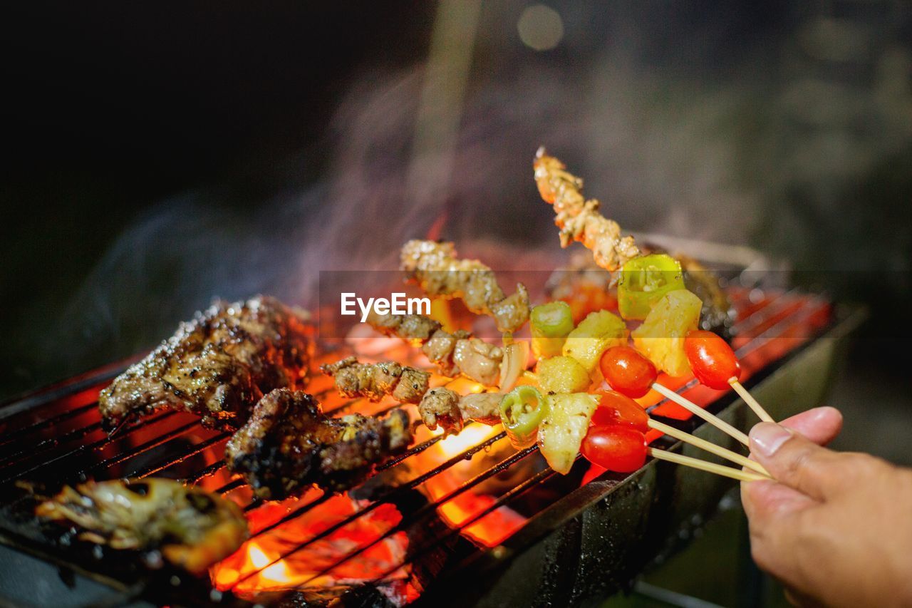 CLOSE-UP OF PERSON PREPARING FOOD ON BARBECUE