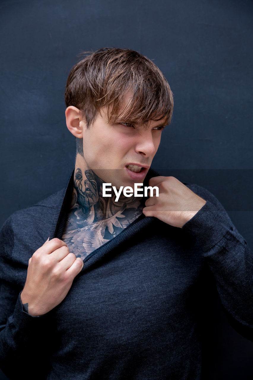 Angry young man with tattooed chest against black background