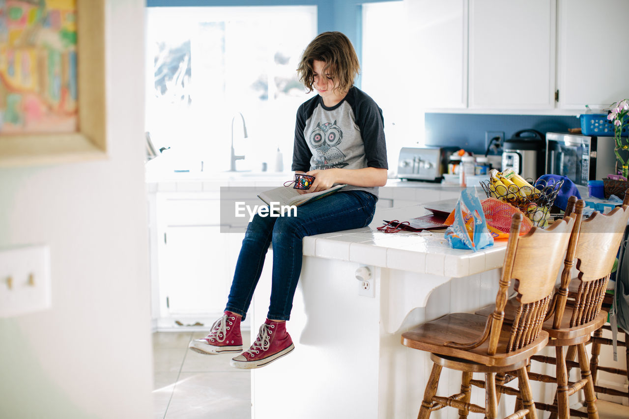 Teen girl sits on kitchen counter and places her bookmark in her book